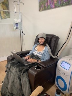 Brett sits in a chair in a treatment room, a cold-cap on her head