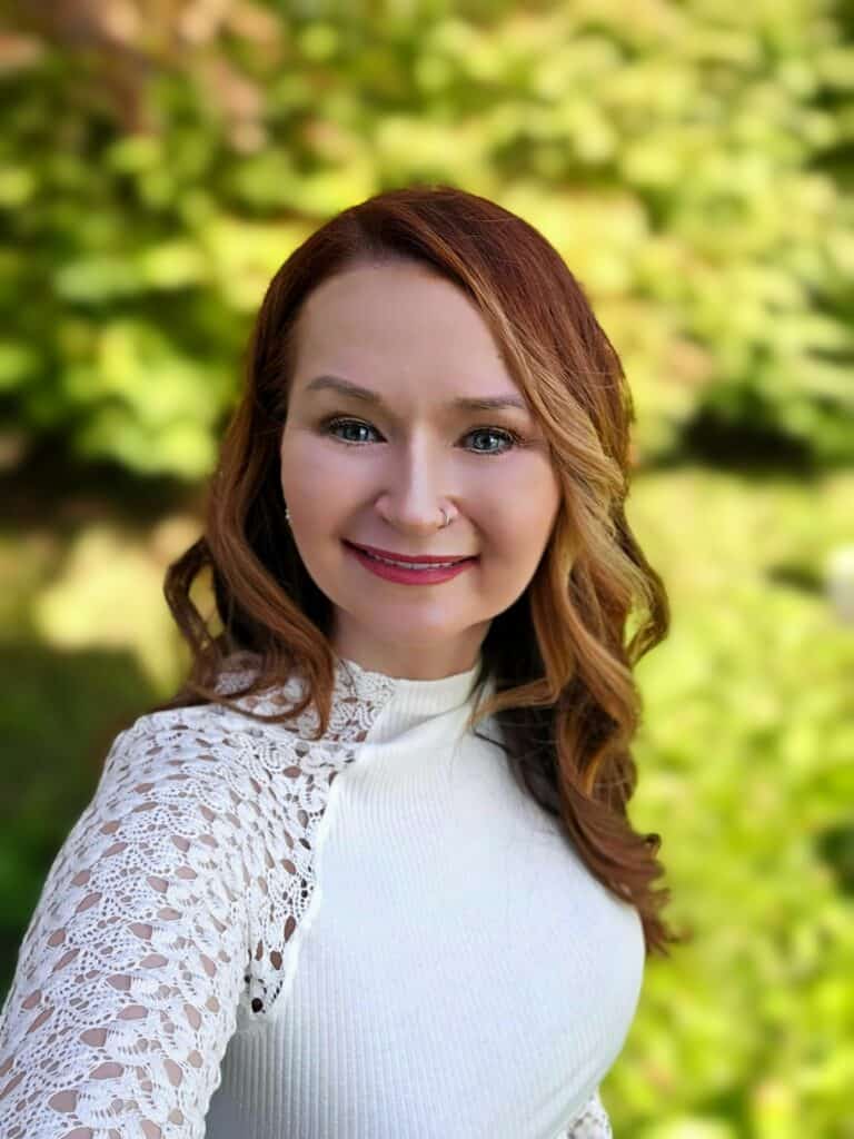 Laura, who successfully advocated for her health, smiles in front of a yard full of green leaves.