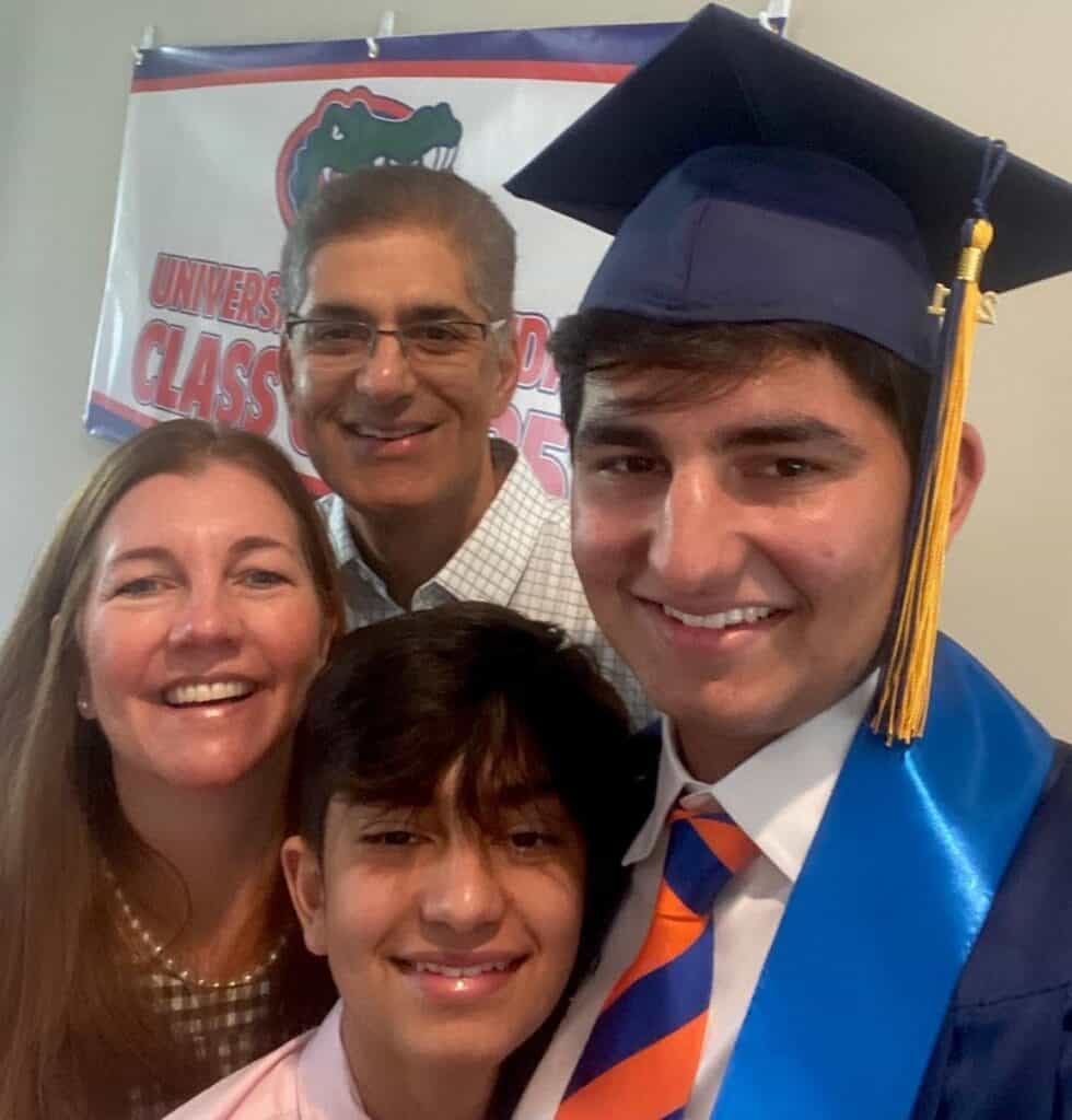 A graduate in cap and gown poses with family members in front of a University of Florida banner. They are all smiling and appear joyful.