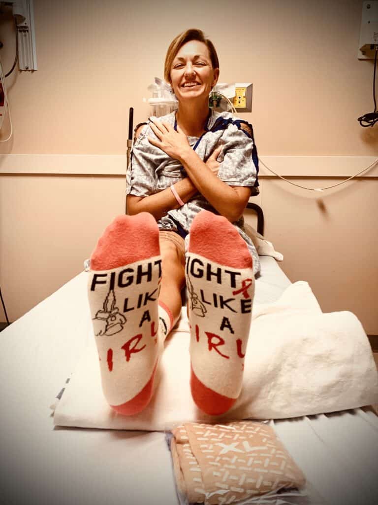 Breast cancer survivor sits in exam room smiling and wearing socks that say Fight Like a Girl