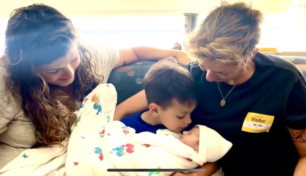 Lisa and her wife smile as their older son holds his newborn baby brother.