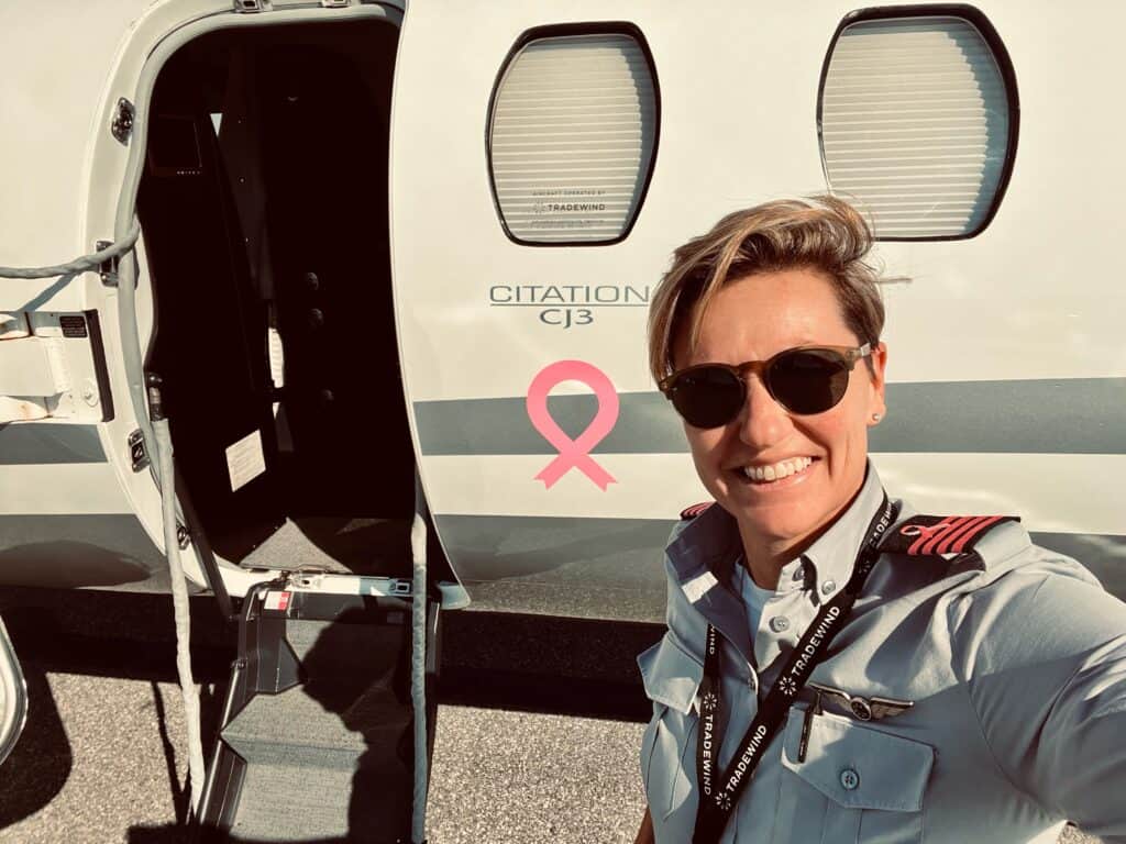 Breast cancer survivor Lisa, in her pilot's uniform, standing in front of an airplane that has a pink breast cancer ribbon painted on it. 