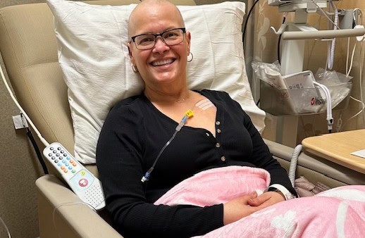 Monica, who is bald, is in a hospital room receiving treatment for breast cancer. 