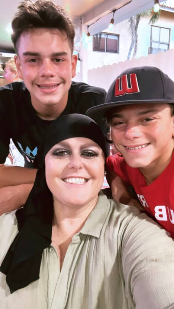 Breast cancer survivor Natalie wears scarf on head and smiles with her twin sons