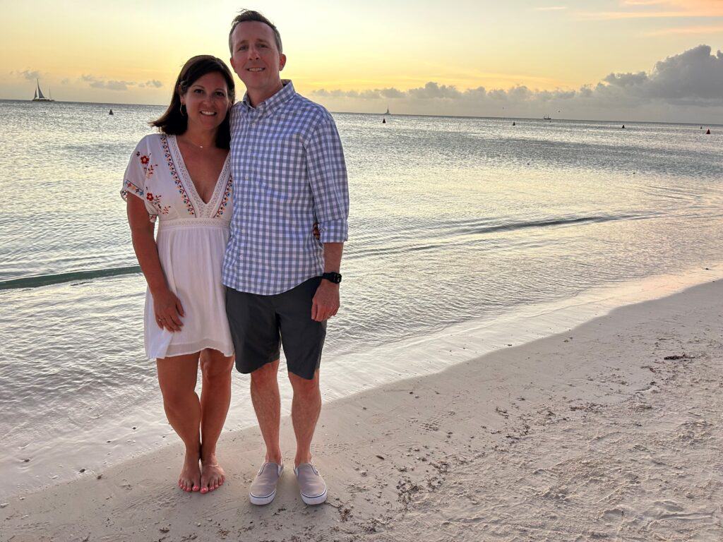 Serena and her husband stand on a beach, their arms around each other.